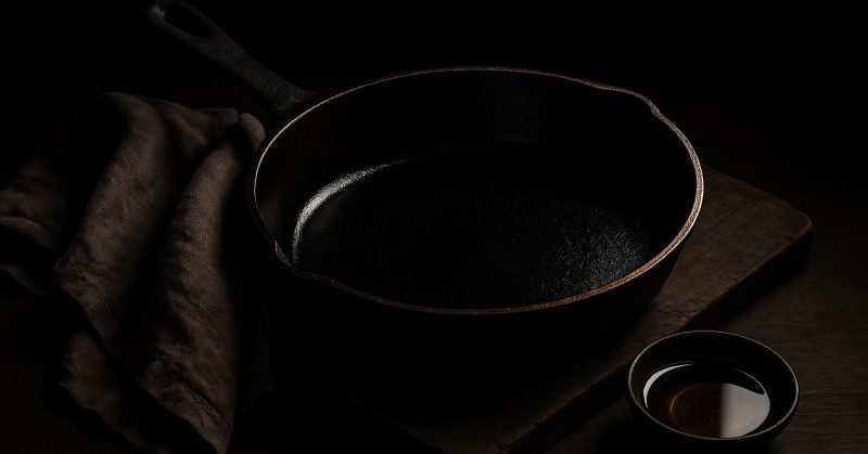 A seasoned cast iron skillet with a cloth and a small dish of oil